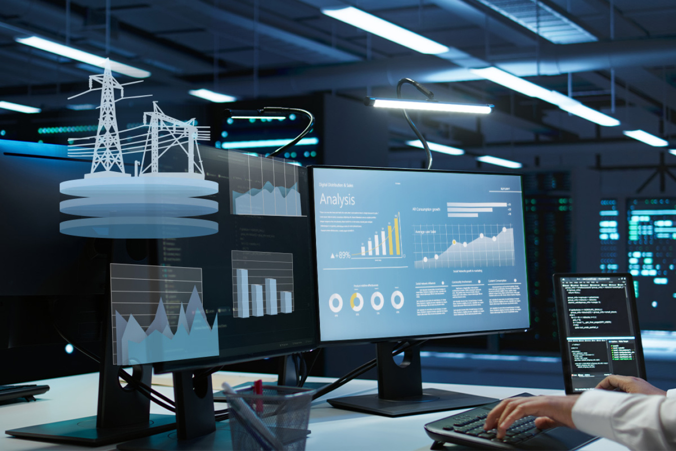 Hands on a keyboard in front of a large computer monitor and smaller monitors in a large control room.