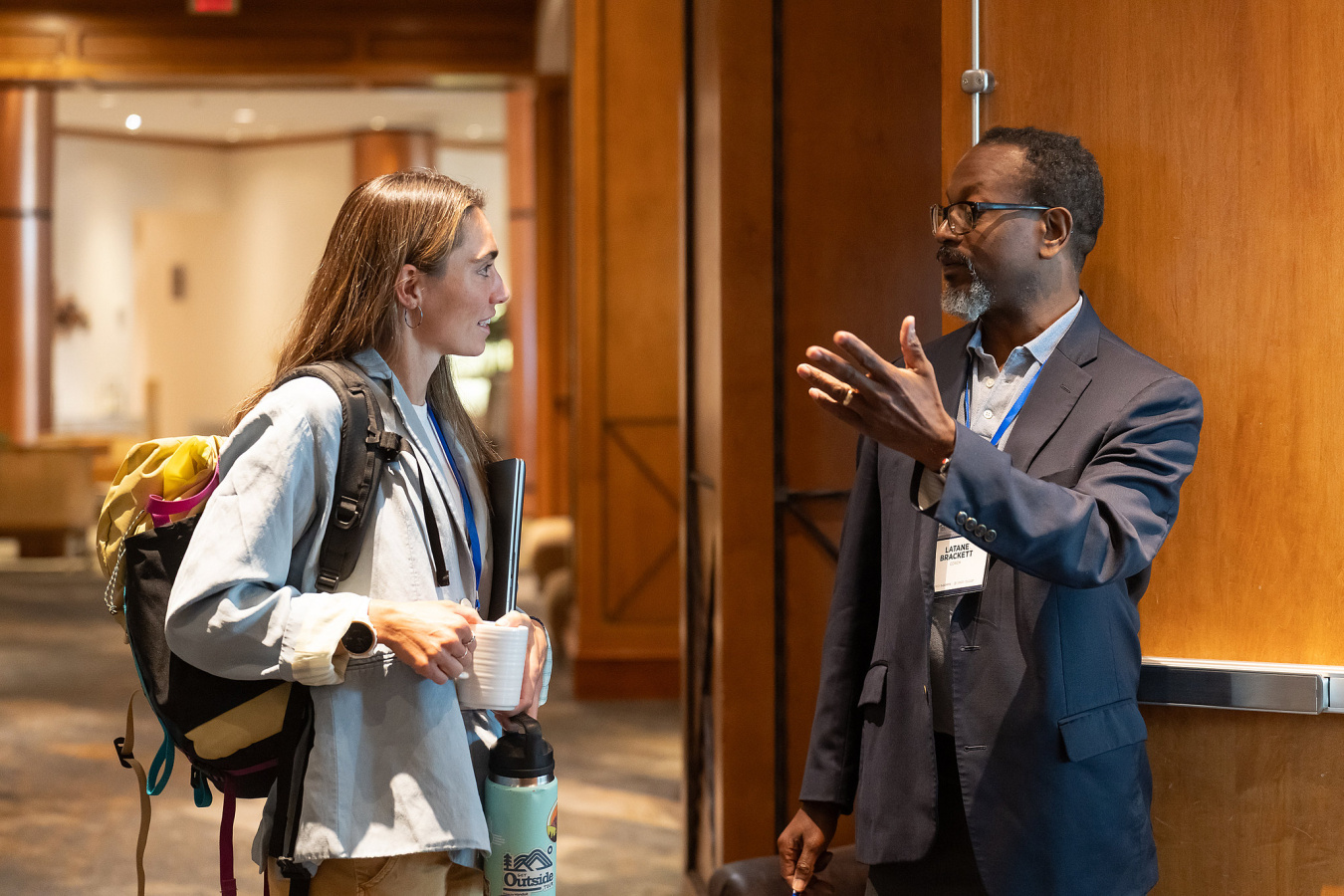 A woman and a man engage in lively dialogue in a conference room setting.  