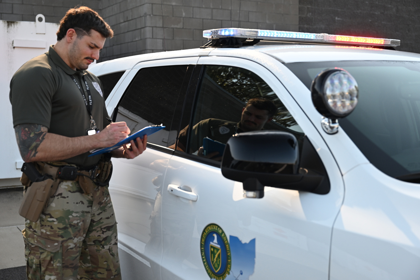 A protective officer at the Paducah site standing beside a white patrol car while holding and looking at a clipboard