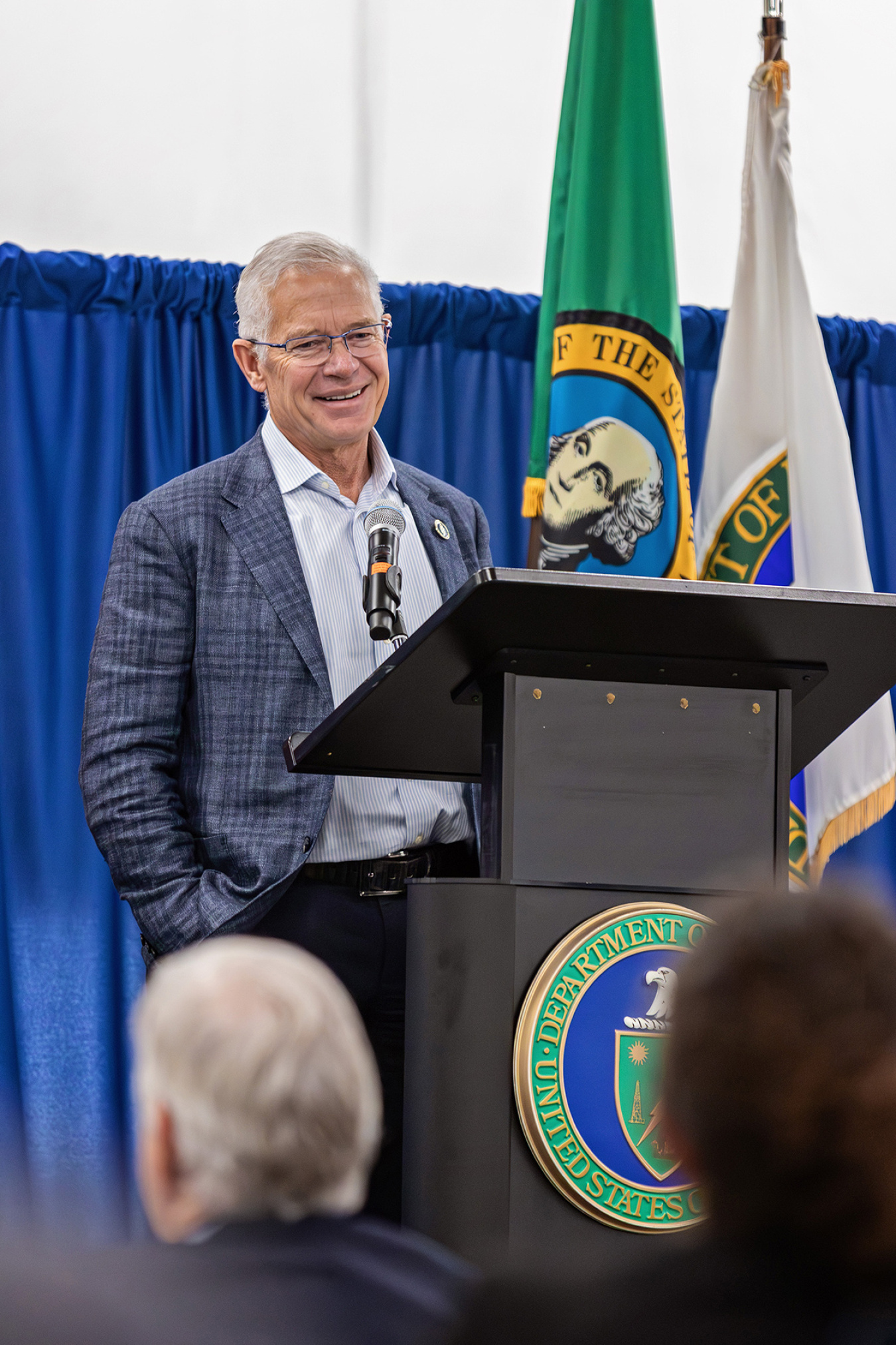 A man in a suit standing behind a podium on a stage smiling at the audience