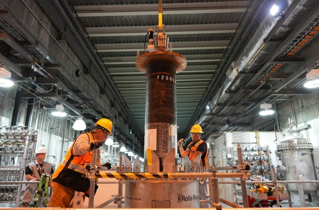 Employees in protective gear standing beside a large flow filter inside a facility building