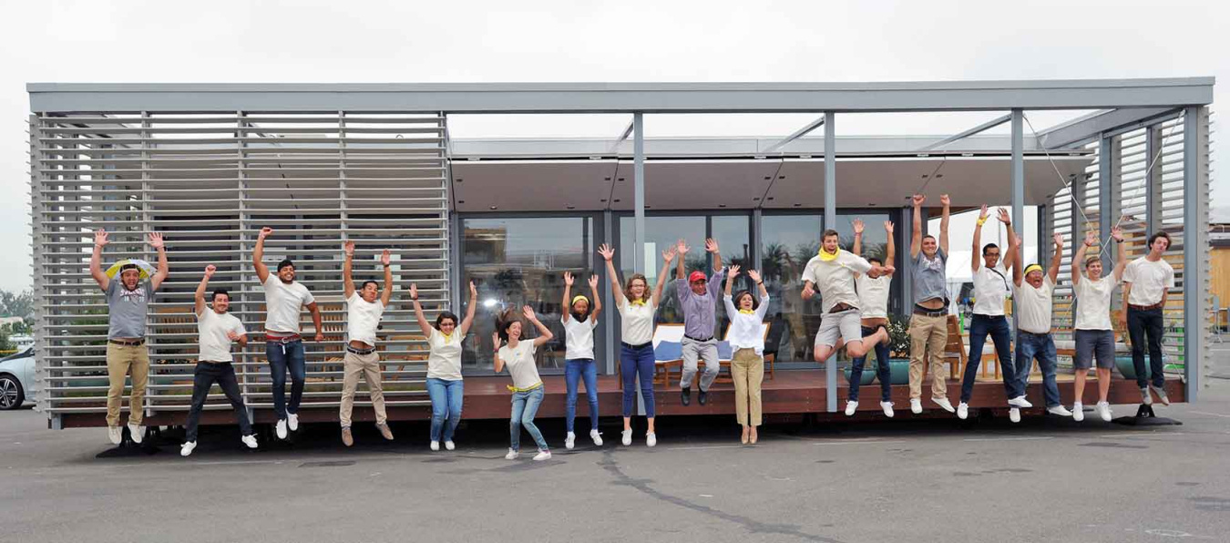 A group of students from a Build Challenge team jumping up in the air, facing the camera, in front of their competition house.