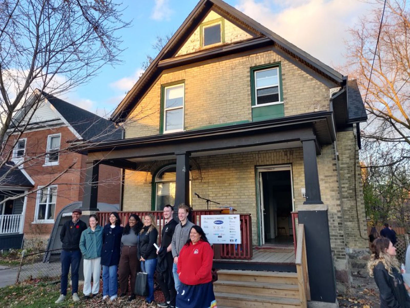 Group of eight people standing together (this team), facing a point off-camera, with their team house behind them.