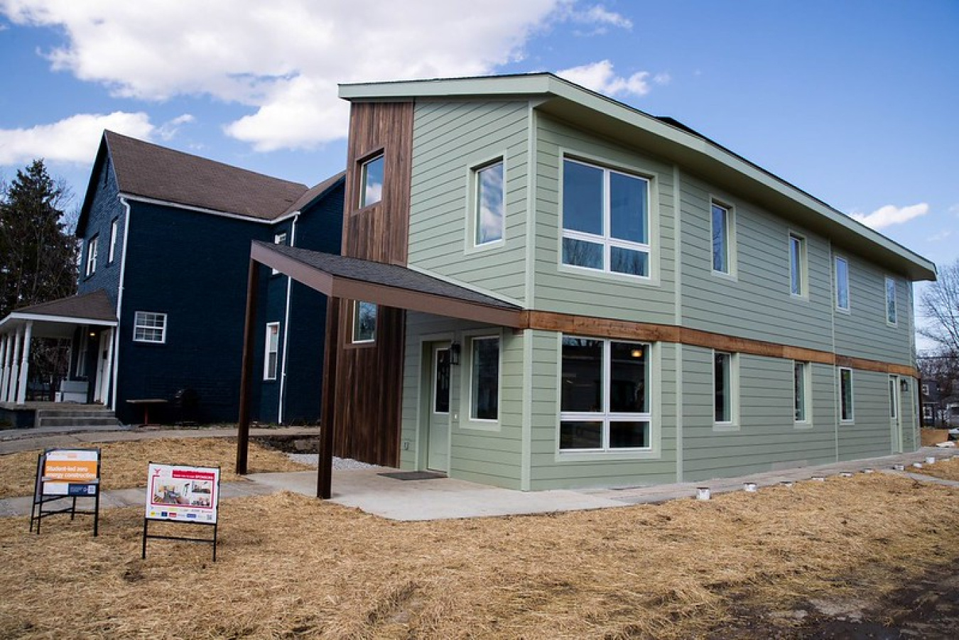 Exterior photo of a two-level house with a couple signs on the lawn in front of it.