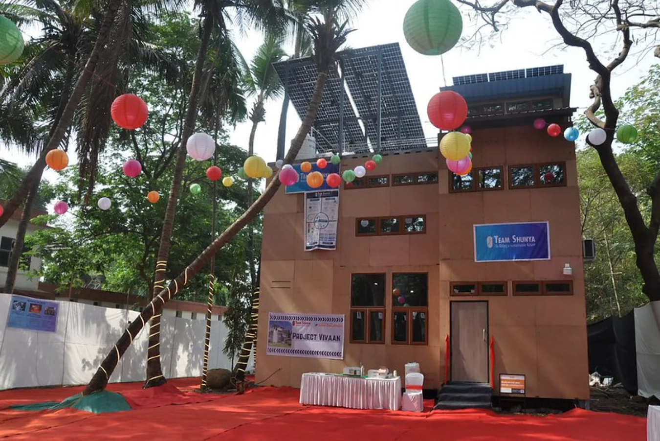 Exterior of a two-level house with modern features and party-like decorations in front of it, with trees overhead and around it.