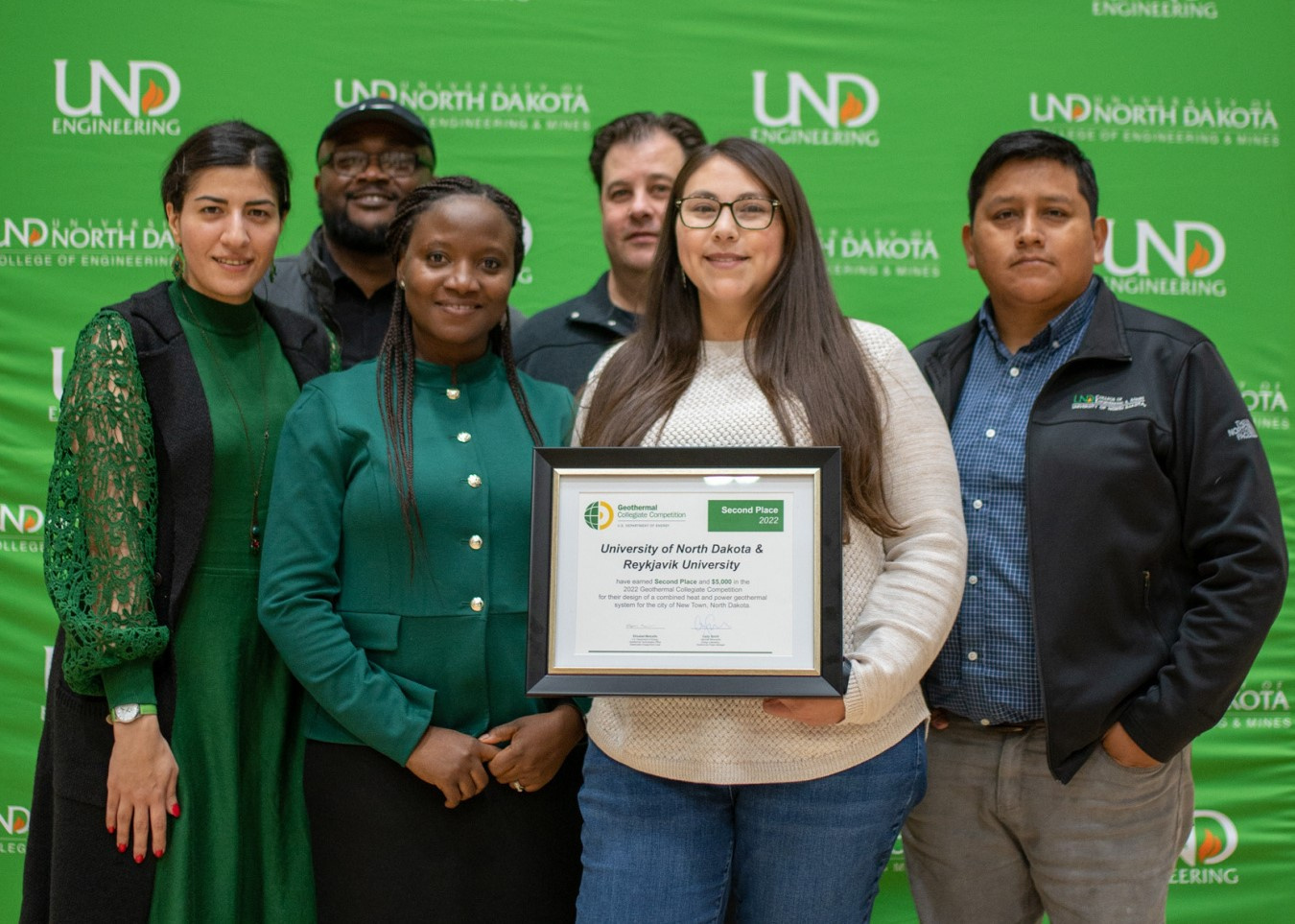 A group of six grad students poses for the camera holding their framed winners certificate