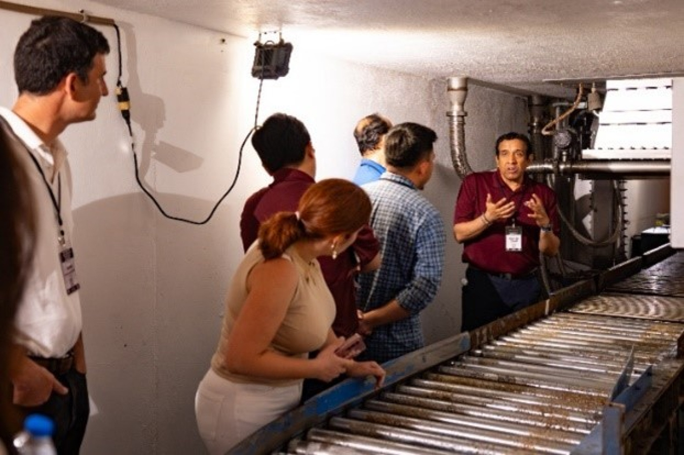 People stand by a conveyor belt used in eBeam sterilization as a man explains the process.