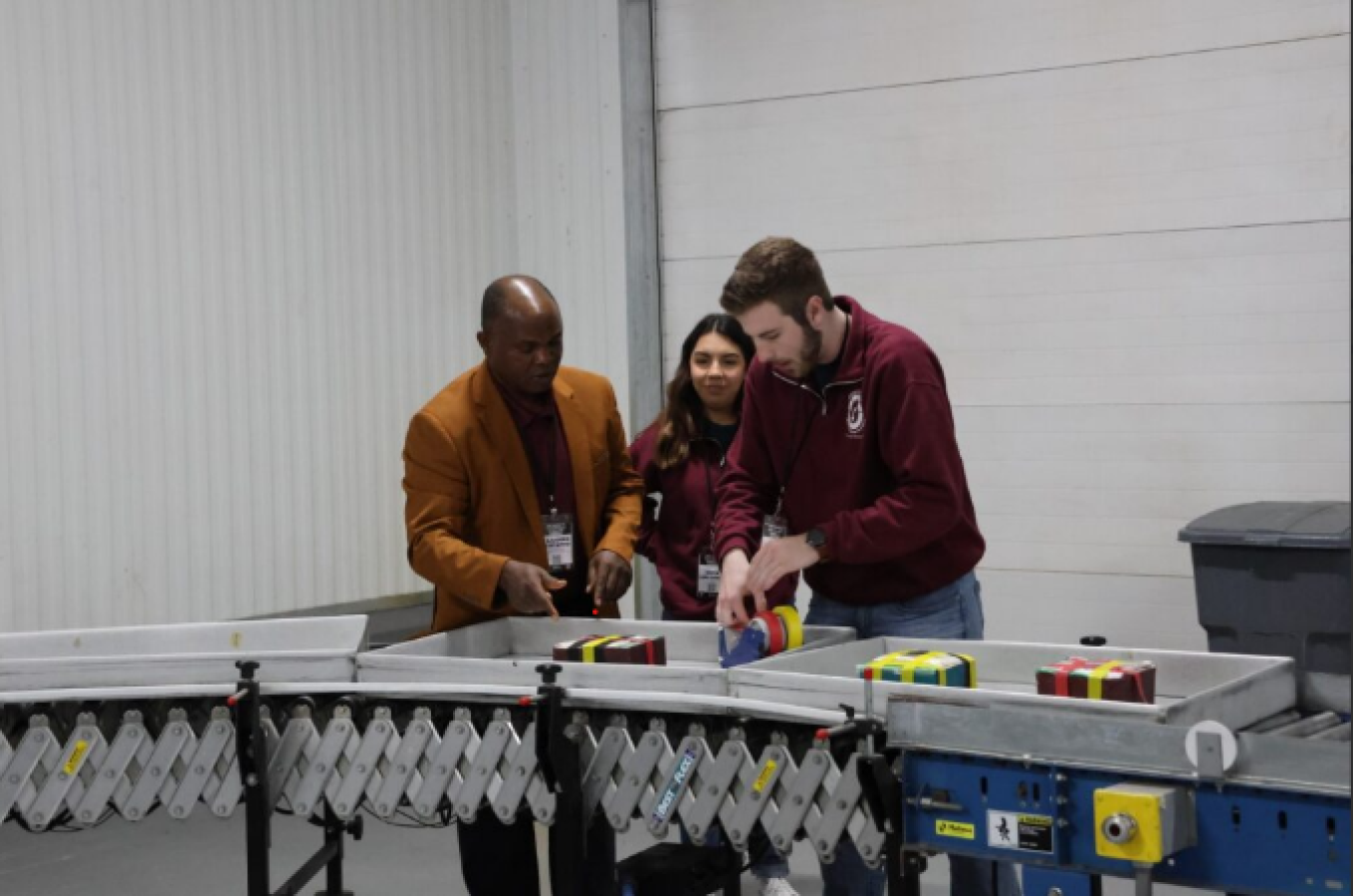 Two men and a woman handle packages on a conveyor belt used in eBeam work.