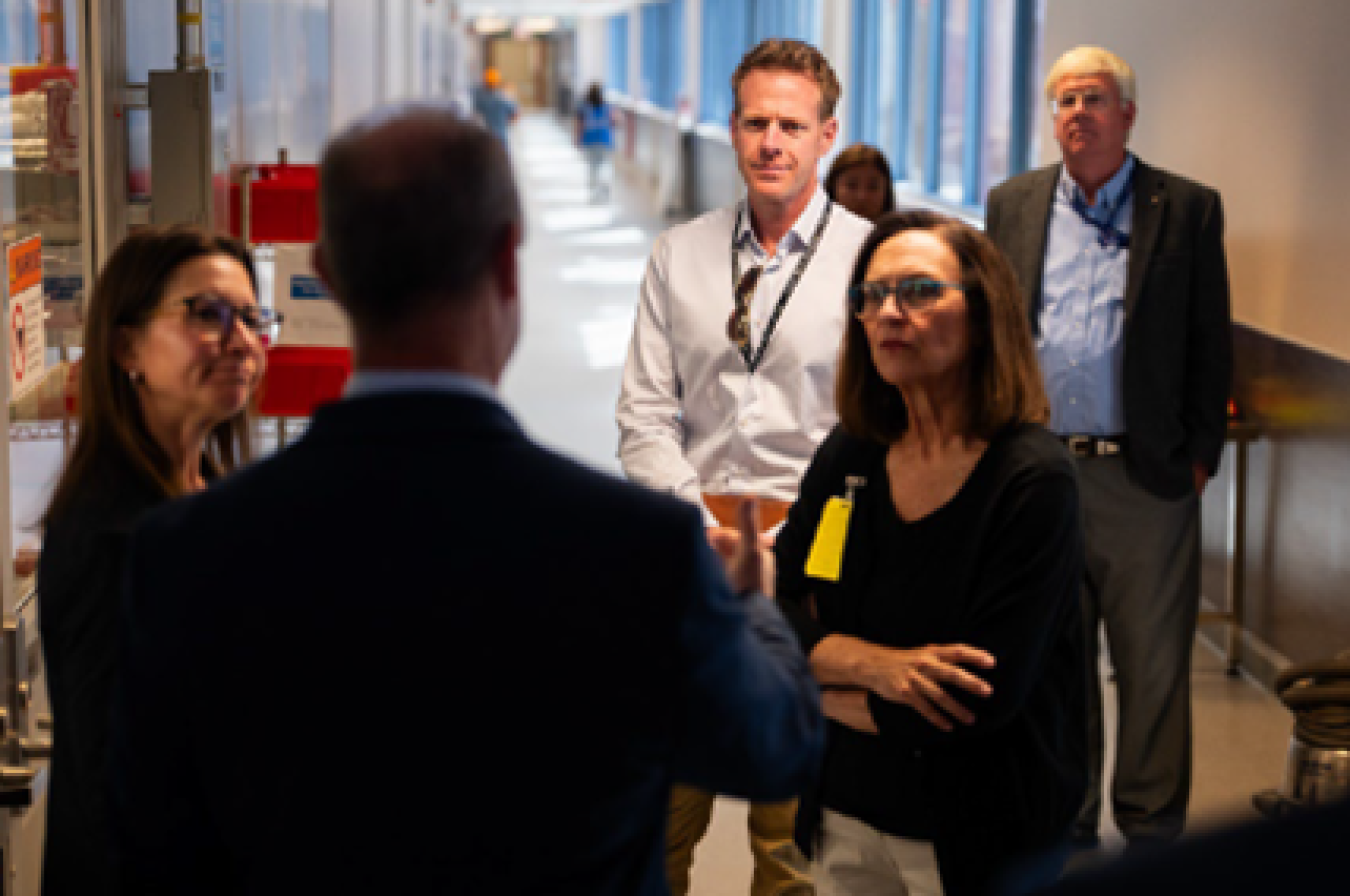 With the focus on a woman in the foreground, a group of people listen as a man explains something.