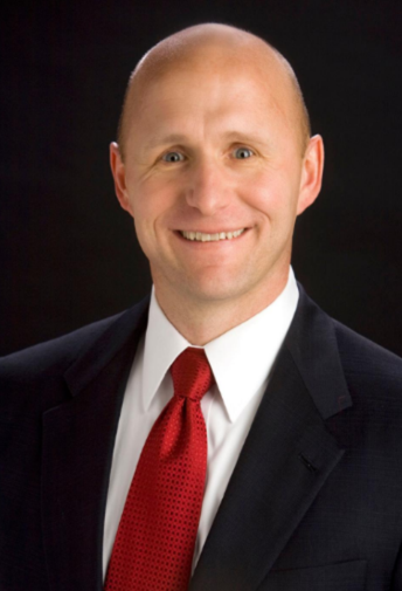 Professional headshot of a man in a suit with a red tie