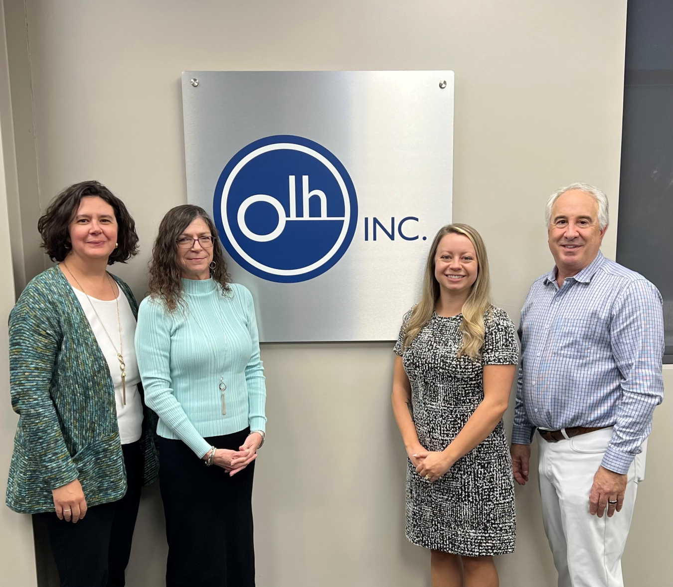 A group of four professionals posing for a picture beside a sign that reads "Olh Inc."
