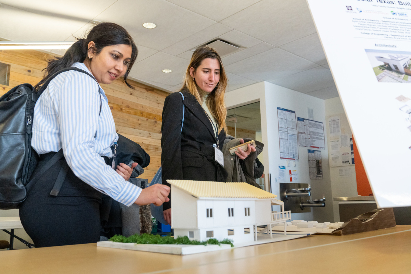 Two women standing at a table looking at a model of a house created by one of the competition teams.