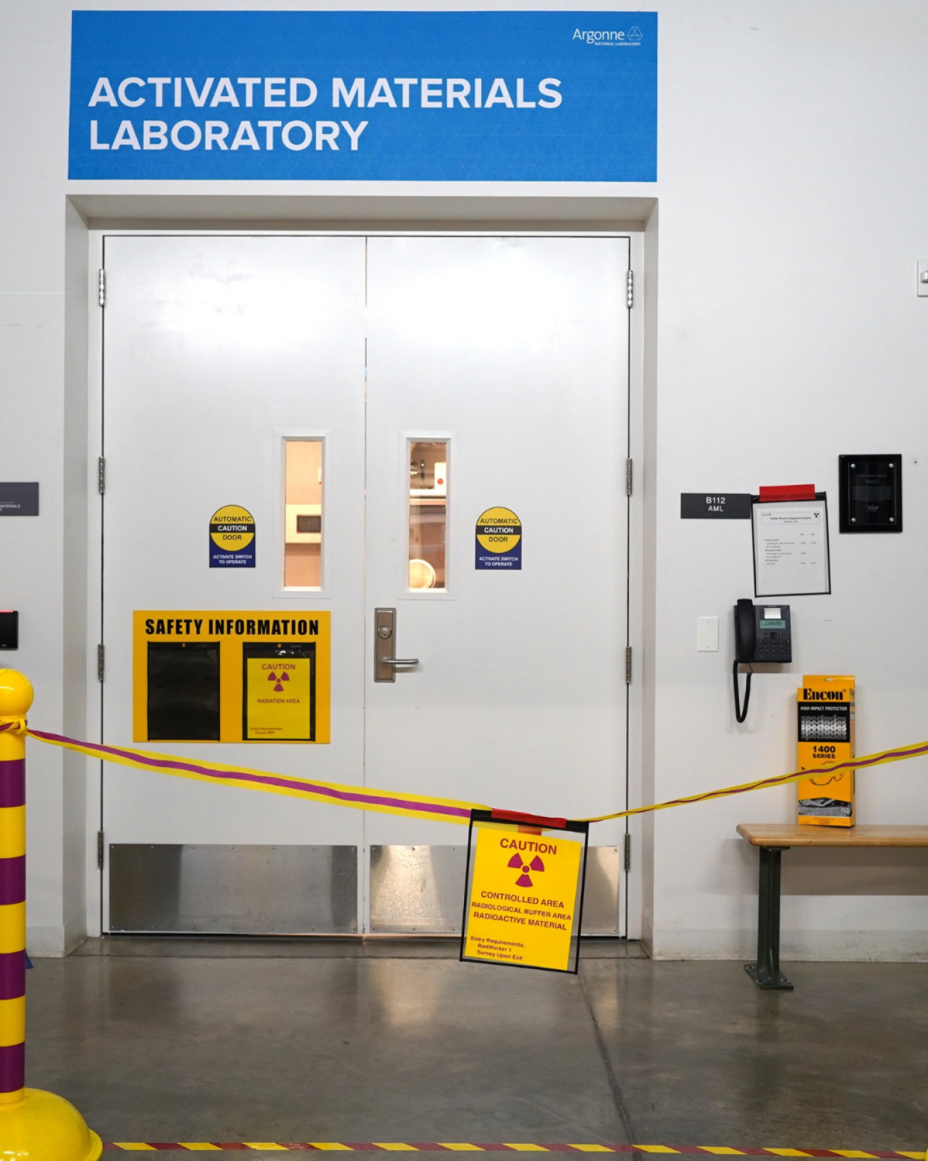 White doors with radioactive warnings and a blue sign with white text reading "Activated Materials Laboratory"
