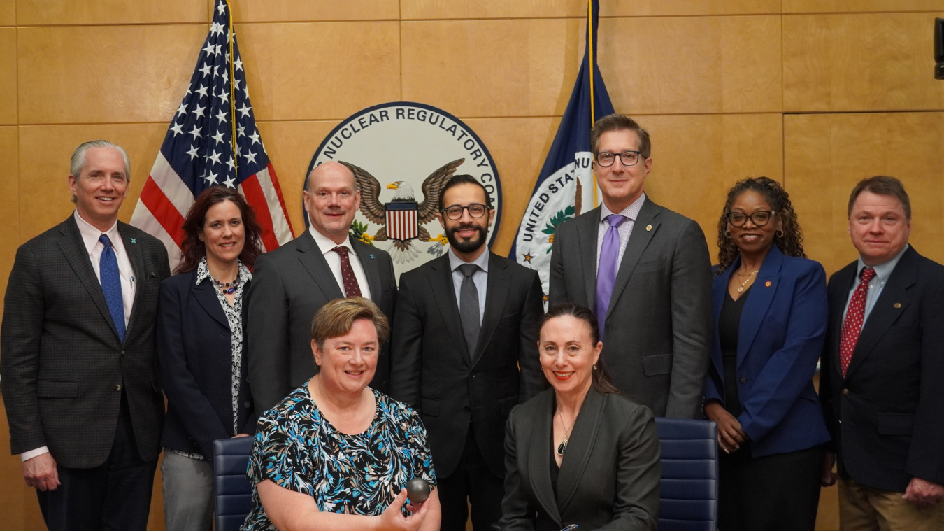 A group of people wearing suits poses in front of the U.S. Nuclear Regulatory Commission Seal