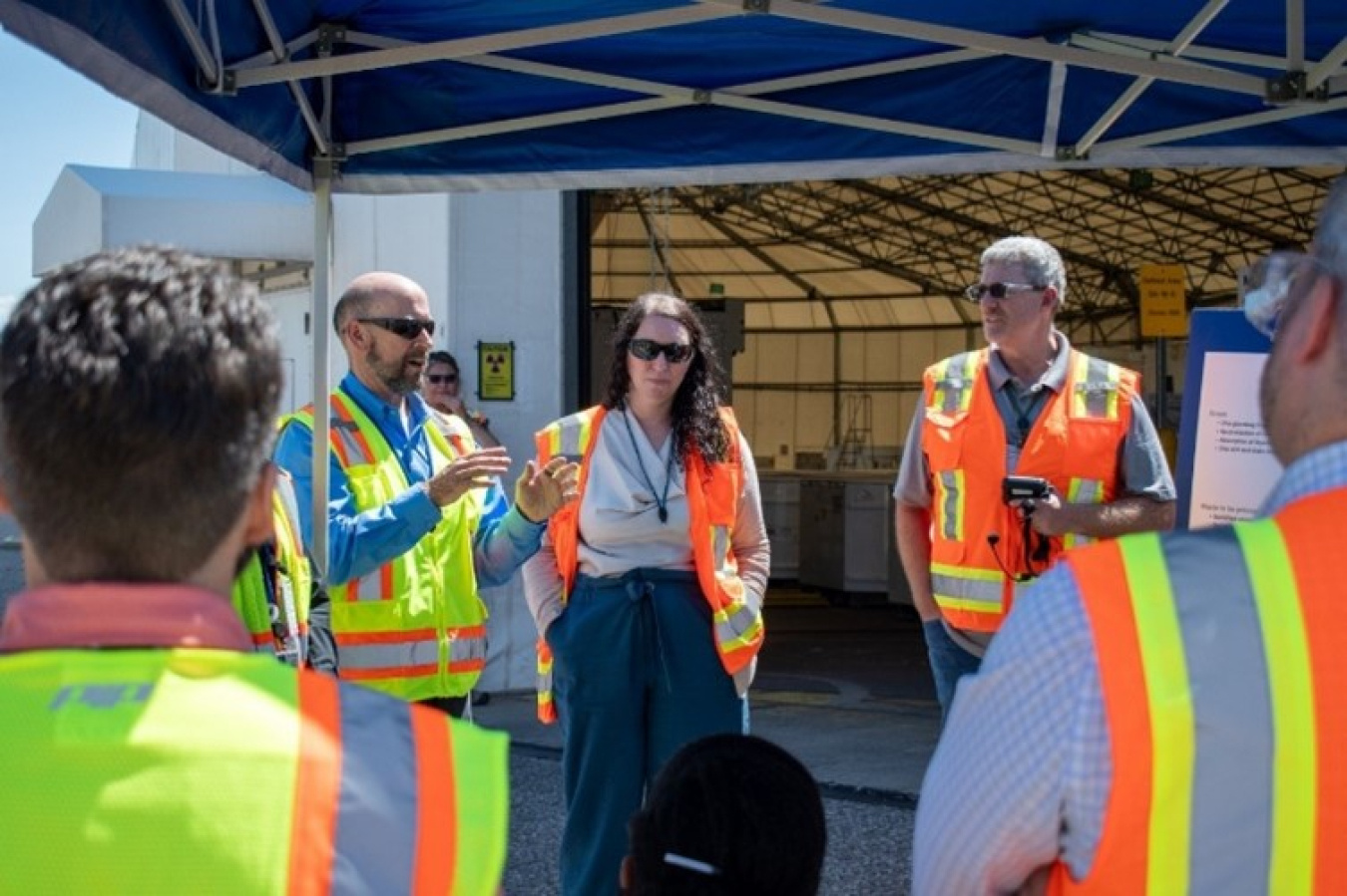 A group of people in reflective vests talking in a circle outside.