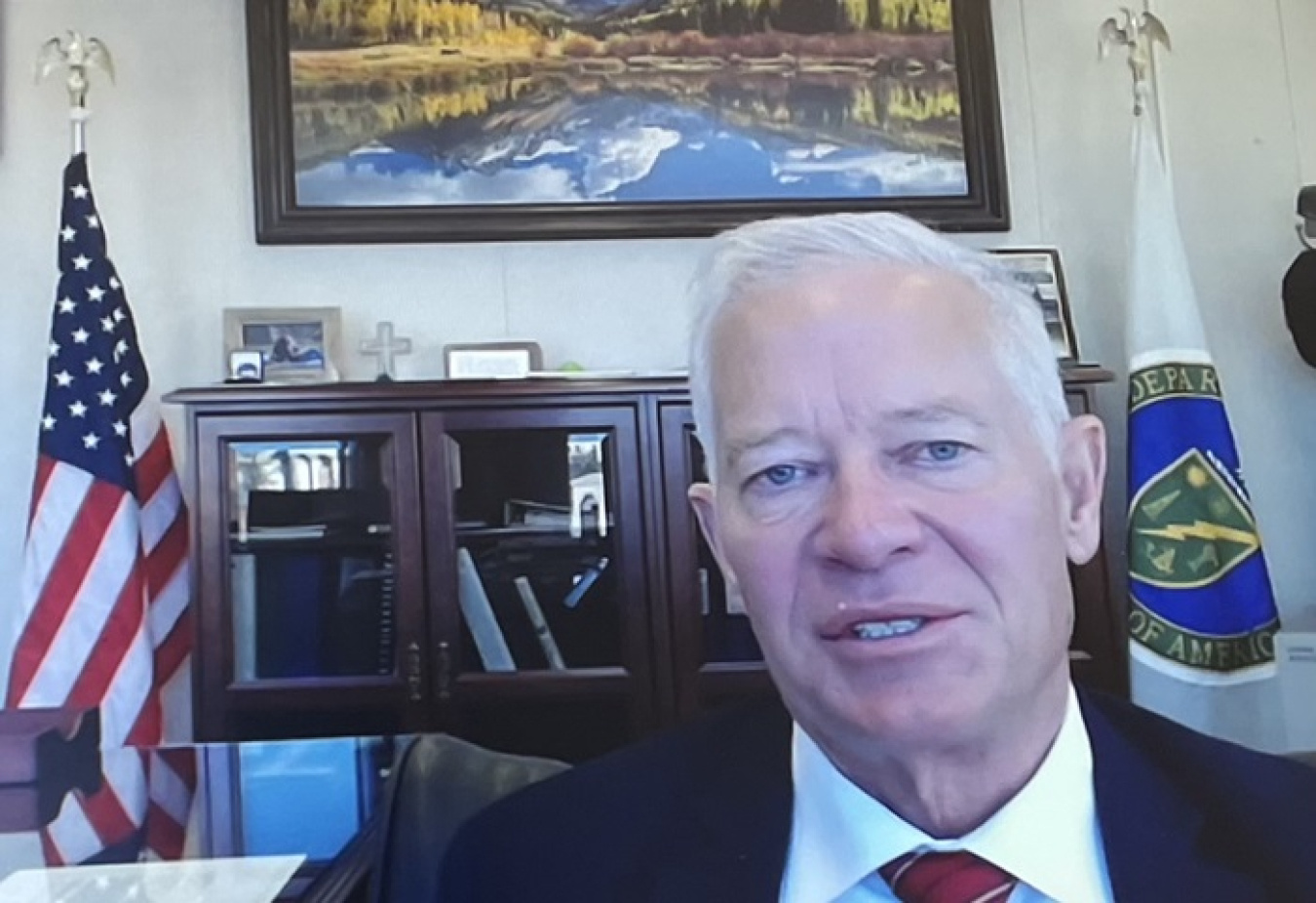 Person facing web camera with US and DOE flags in background