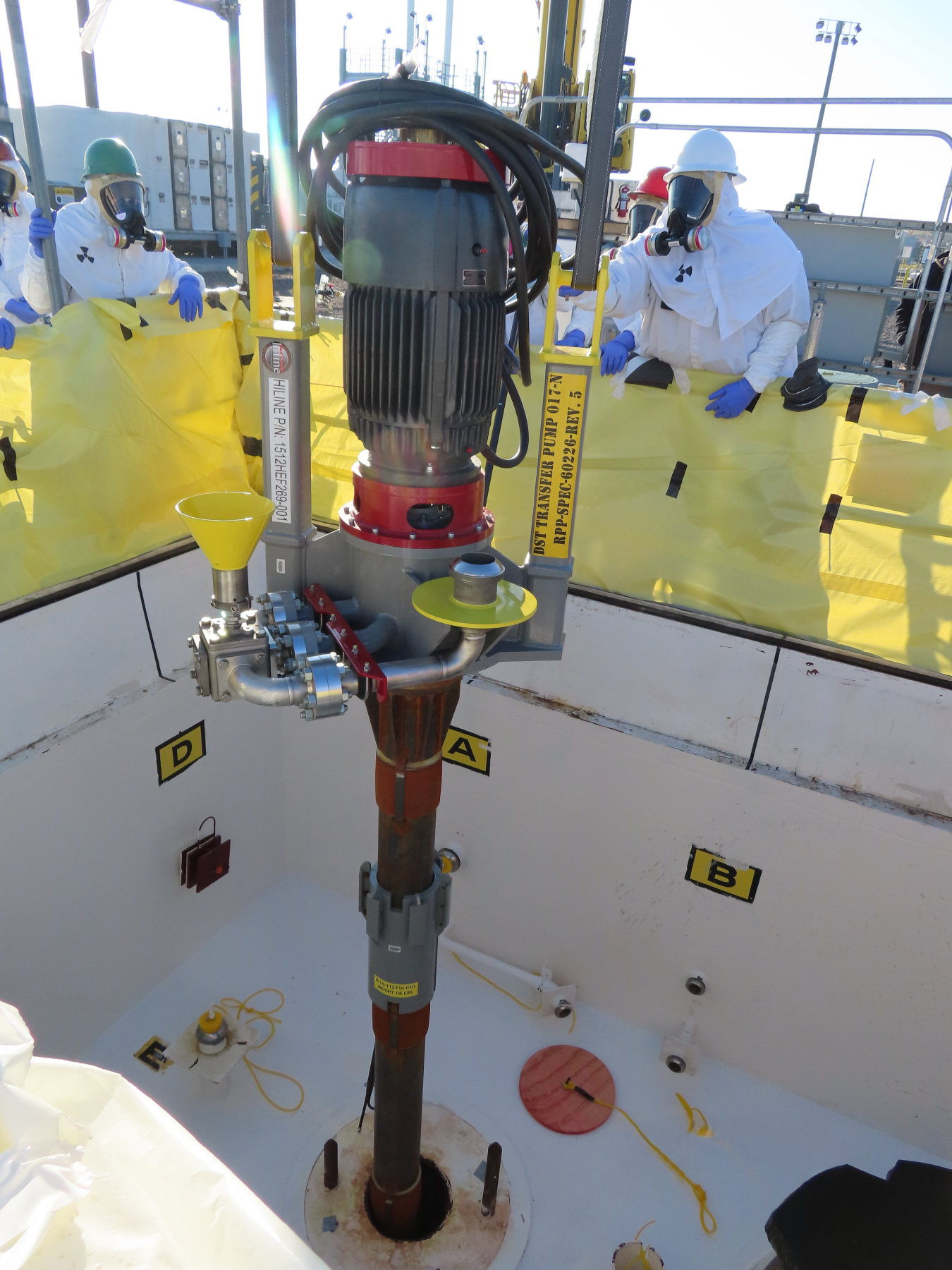 A grey and red pump being installed by employees in protective gear