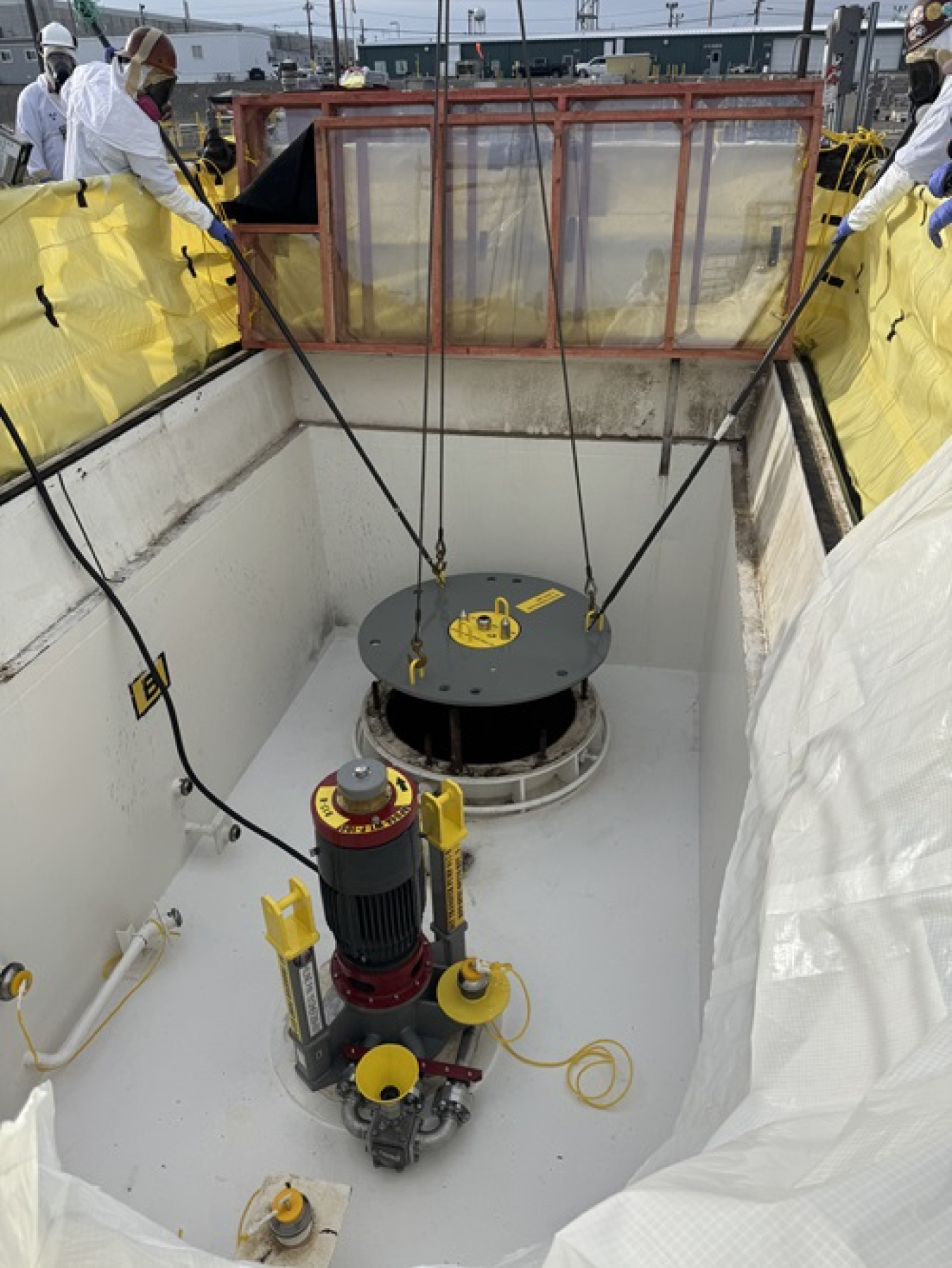 A grey and yellow round slurry disk and red and grey pump installed in the ground