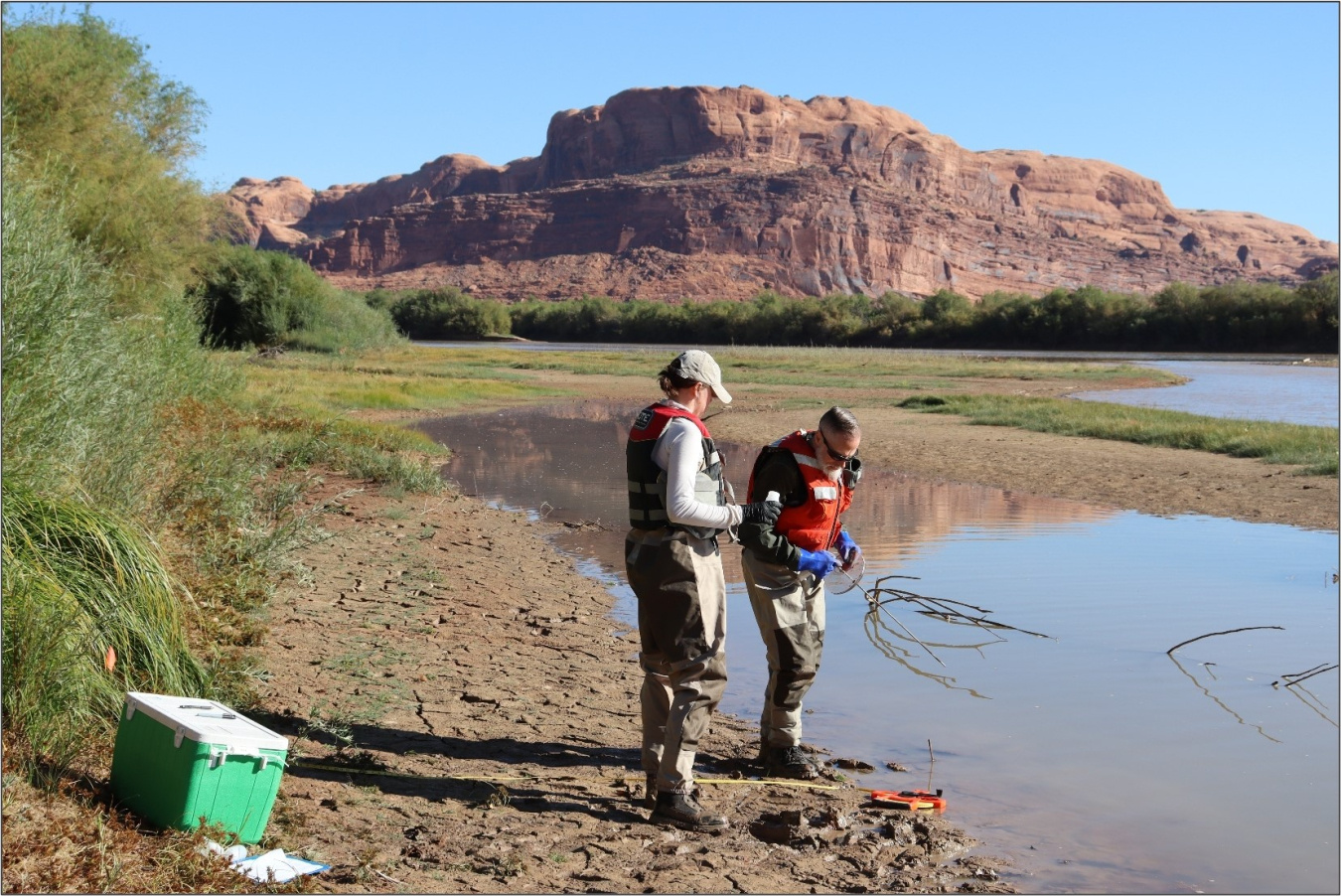 Two employees conducting surveys of the water at a riverbank at the Moab Site