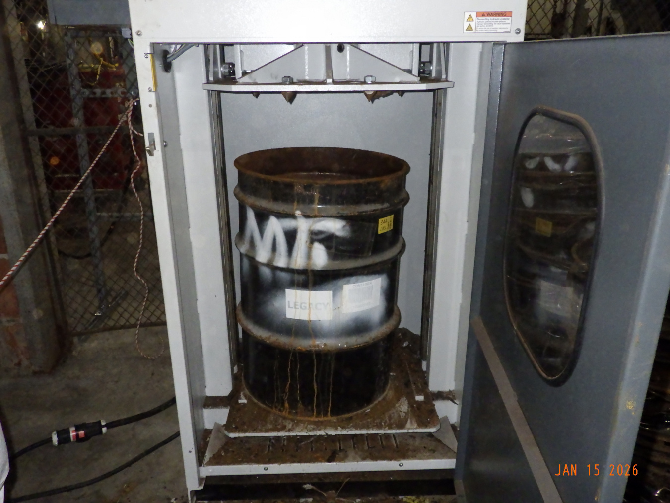 A dark colored waste drum inside a crusher machine at the Oak Ridge Site