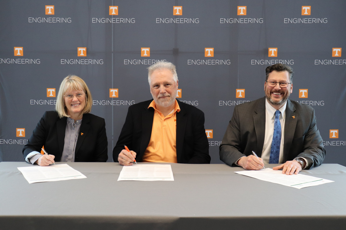 Three professionals sitting at a table smiling for a picture while signing a piece of paper