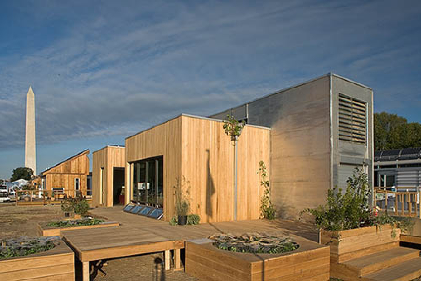 Exterior of the Carnegie Mellon team's Build Challenge house, showing the sun shining on the corner facing the camera, with various sections made of different materials. The Washington monument shows off in the distance, as the event site is in D.C.