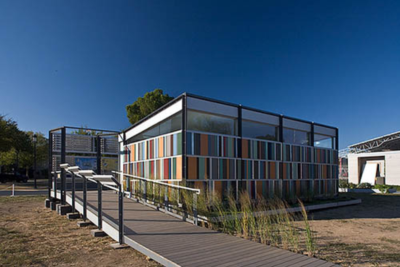 Exterior of the Cincinnati team's Build Challenge house, showing multicolored slats / panels along two sides and a ramped walkway leading up to it.