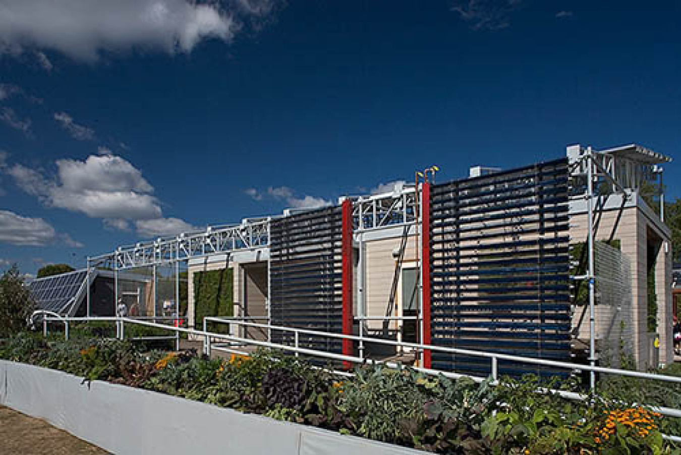 Exterior of the Cornell team's Build Challenge house, showing sections of lattices in different colors and styles along one side, and a railed walkway running along it.