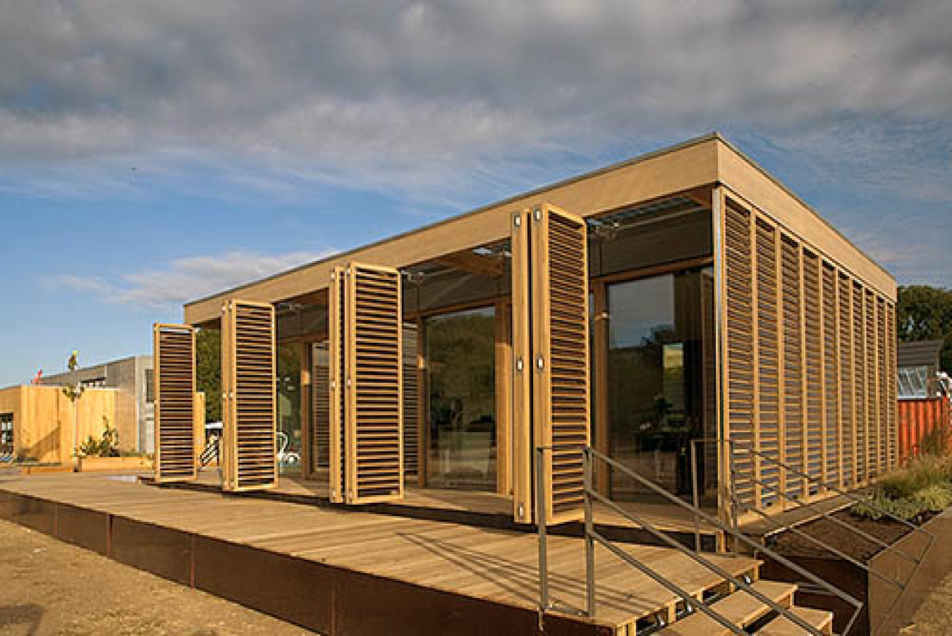 Exterior of the Darmstadt team's Build Challenge house, showing sections of a wood-looking material with accordion doors / shutters along the front, and a wooden walkway /platform in front of it.