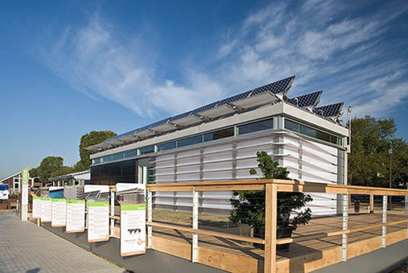 Exterior of the Georgia Tech team's Build Challenge house, showing horizontal slats along the two sides facing the camera, and a wooden-railed walkway in front of it with some display signs.