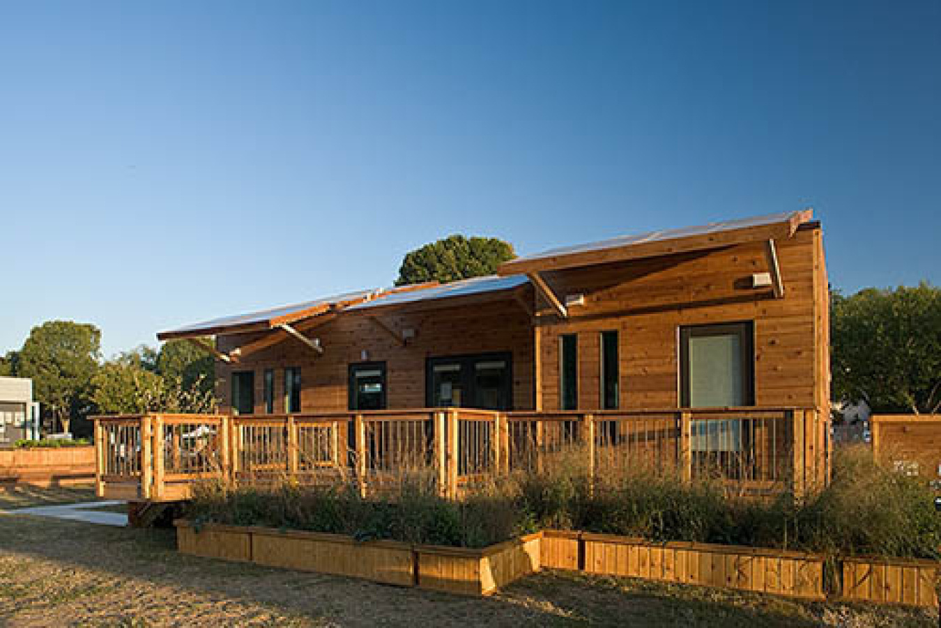 Exterior of the University of Illinois team's Build Challenge house, a wooden structure with overhangs along the front and a wooden-railed walkway.