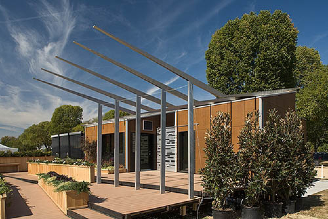 Exterior of the Lawrence Tech team's Build Challenge house, a structure with vertical panels along the front, and poles / posts standing along the front with segments jutting out horizontally from the roof.