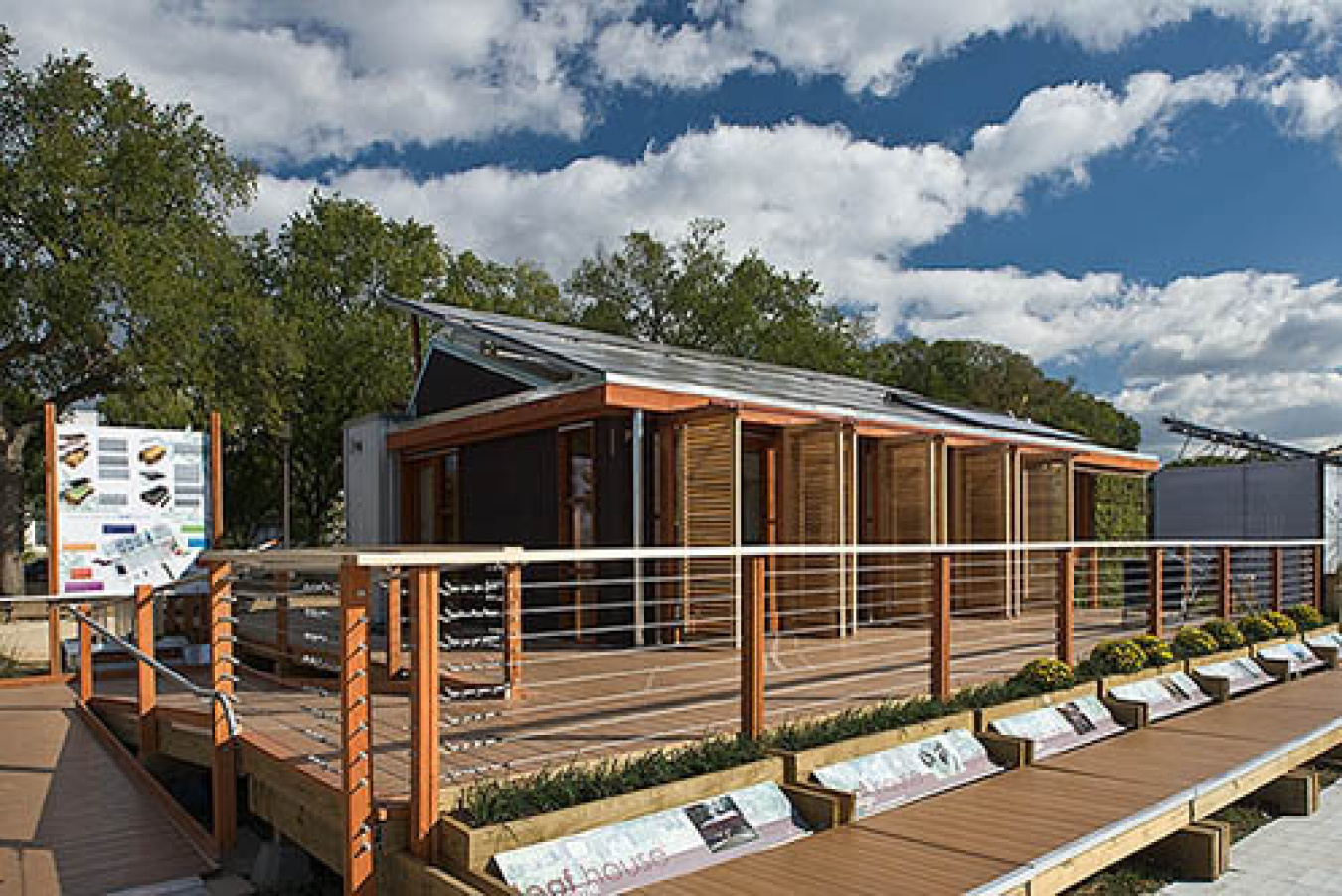 Exterior of the Maryland team's Build Challenge house, a structure with several sections along the front, a railed walkway along the front, and a sign off to the side.