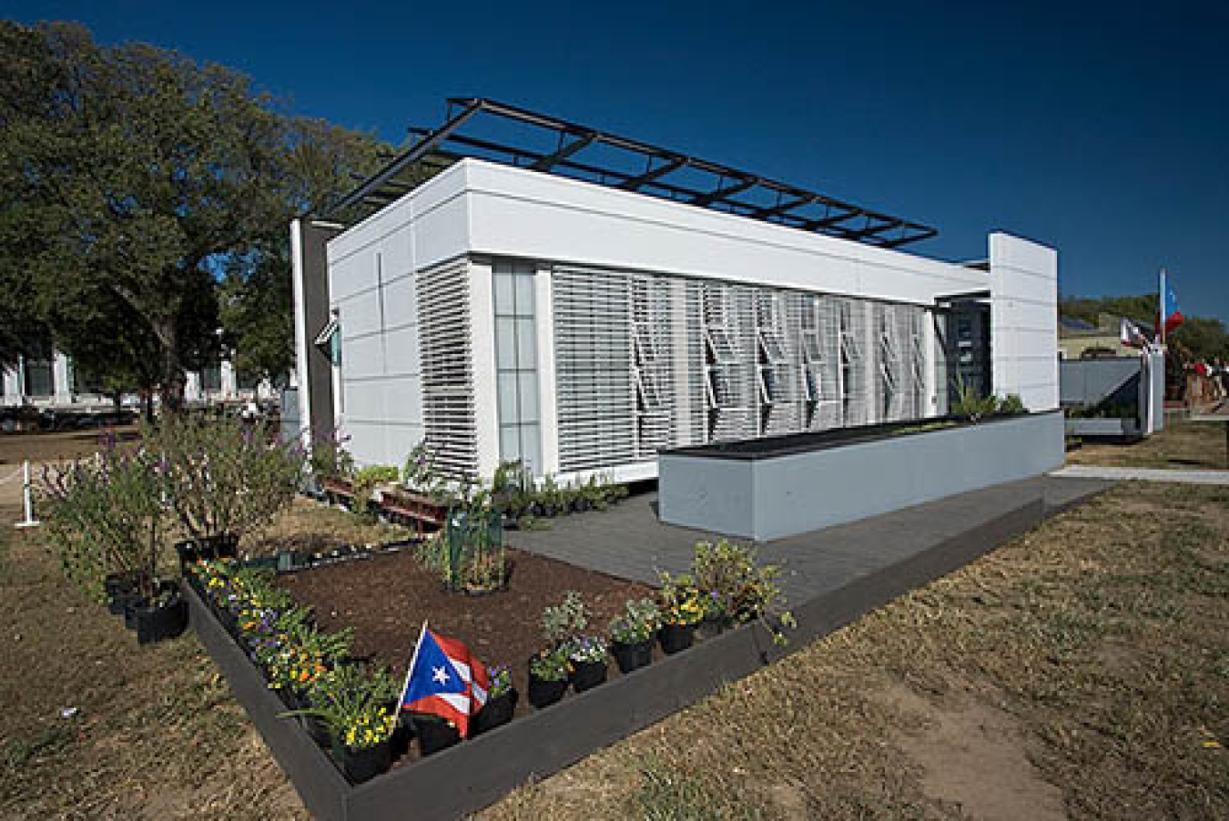 Exterior of the Puerto Rico team's Build Challenge house, a light-colored horizontal structure with grated window panels along the front.