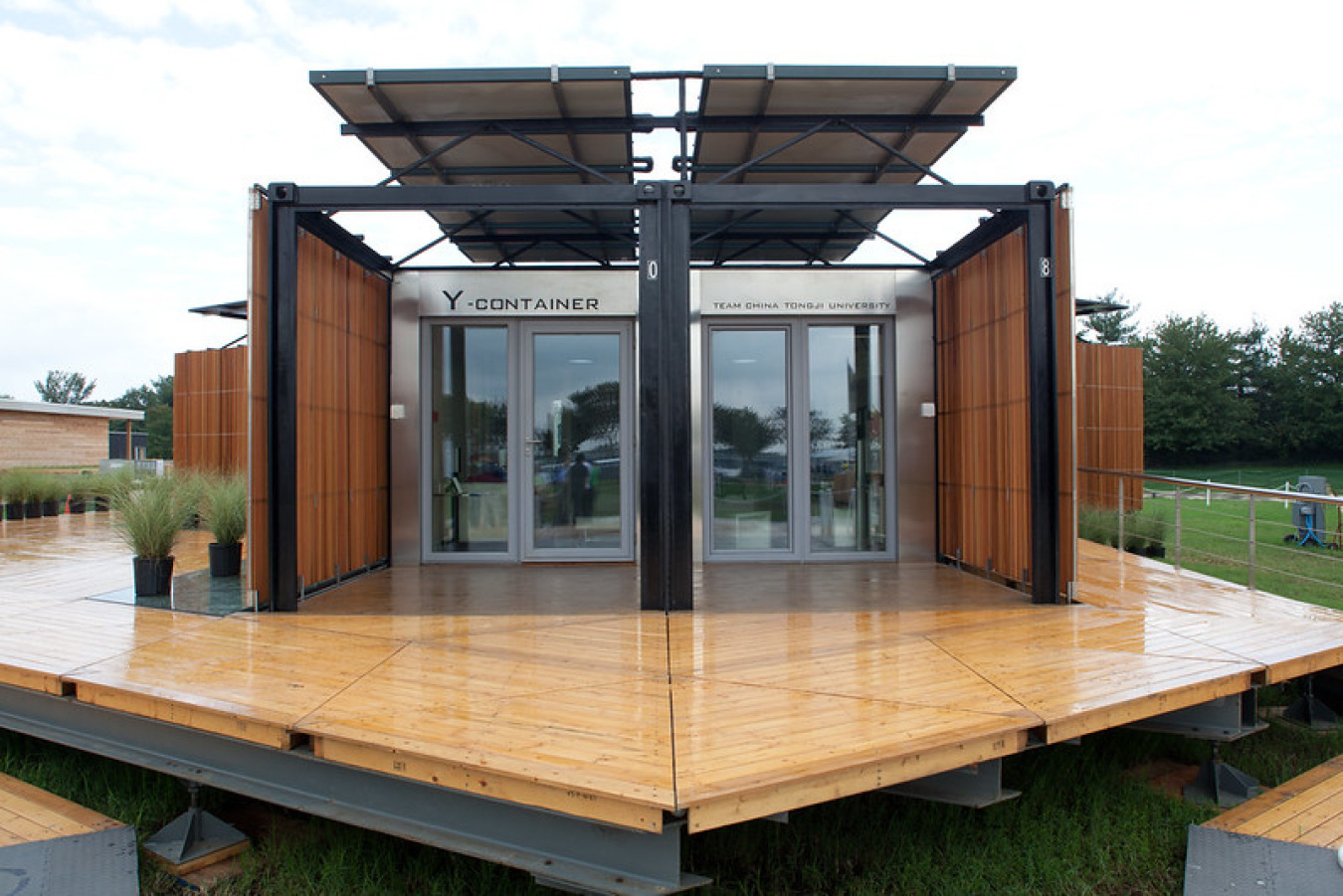 Exterior of Team China's Build Challenge house, showing two identical sections meeting each other in the center, each side having a windowed entrance, and there is a angular platform / porch jutting out in front of it.