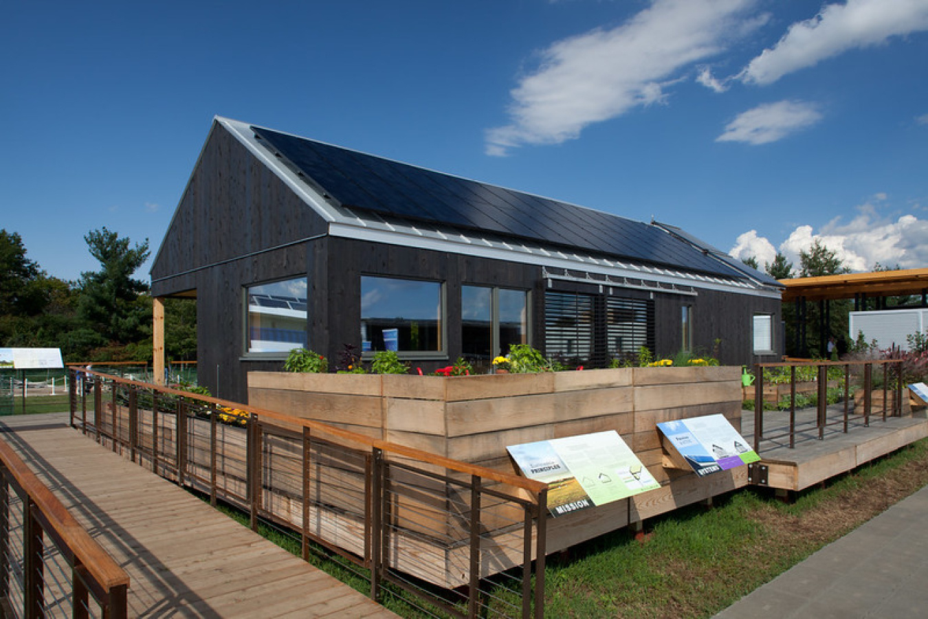 Exterior of the Middlebury team's Build Challenge house, showing a sloped roof over a sided structure with a fenced area around it.