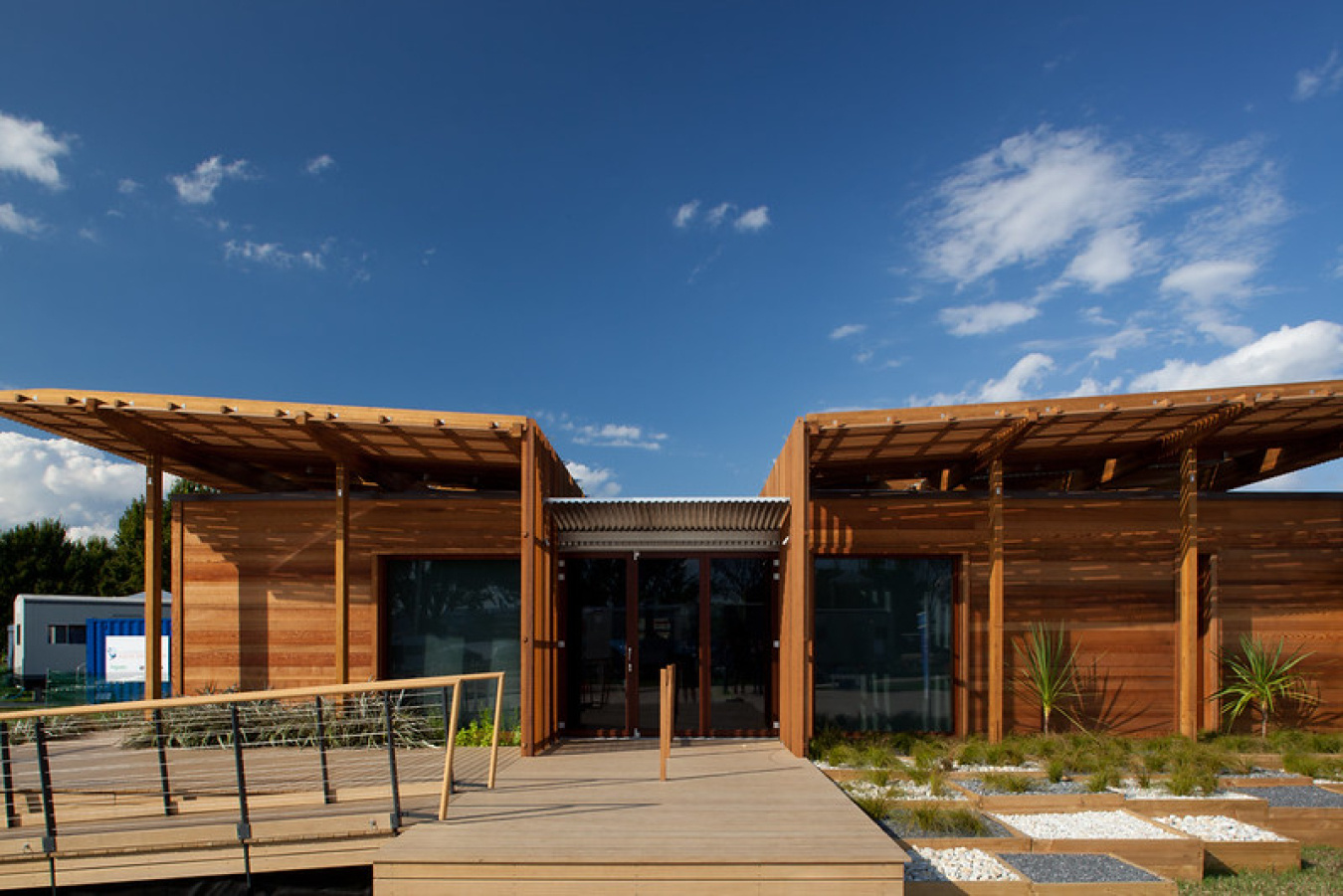 Exterior of the New Zealand team's Build Challenge house, showing a wooden structure with two sections jutting out on each side of the front entrance.