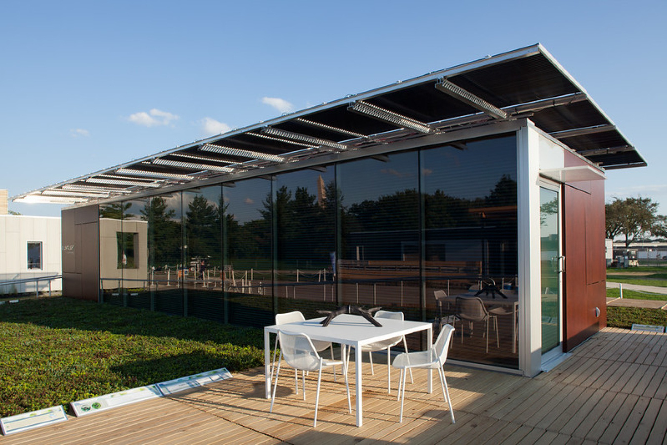 The University of Tennessee team's Build Challenge house, a structure with darkened windows along the front, and a table and chairs sitting on a patio in front of the house.
