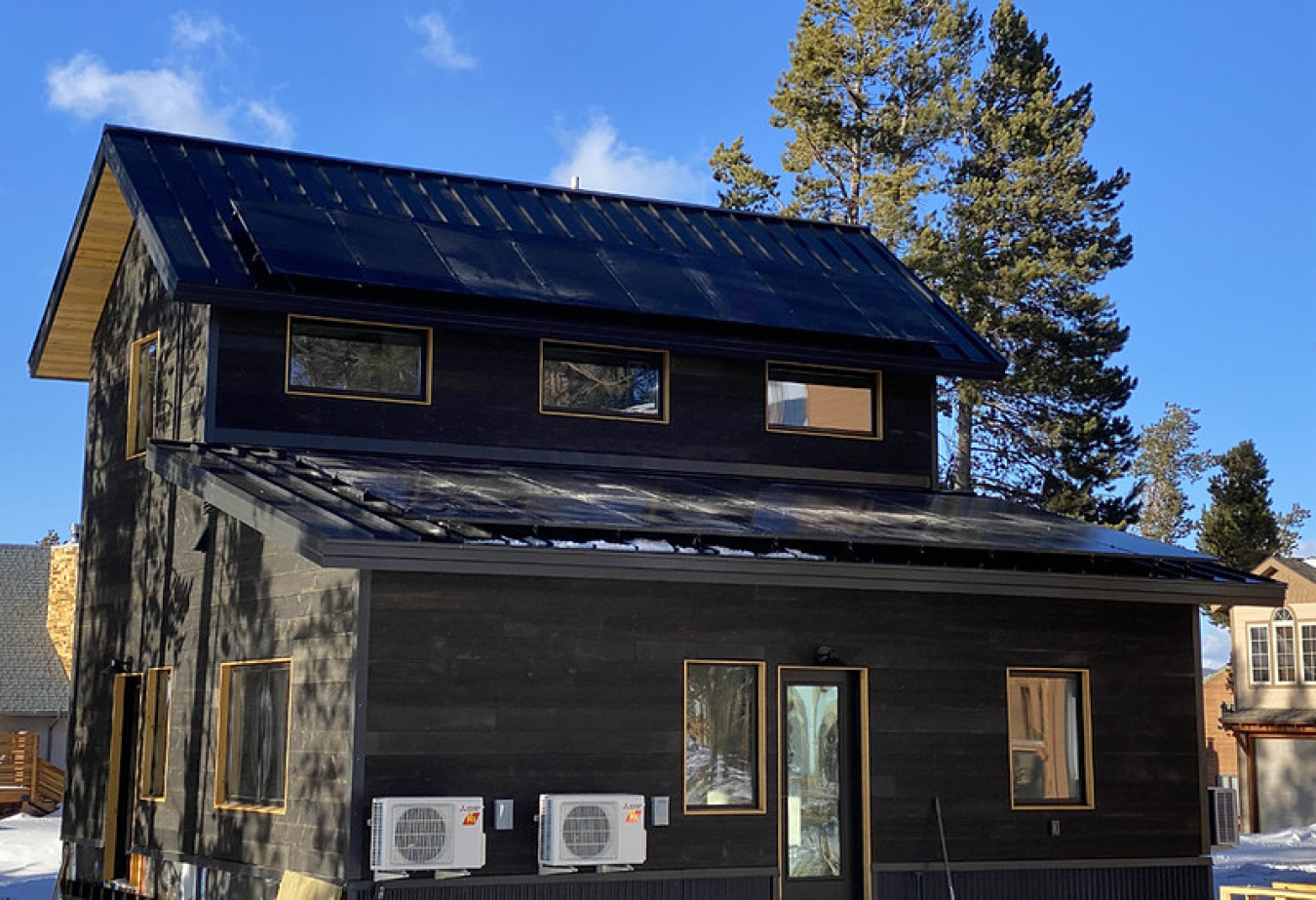 Exterior of the Colorado team's Build Challenge house, a two-story structure with pointed roof and lots of windows, and a couple trees sit on the far side of it.