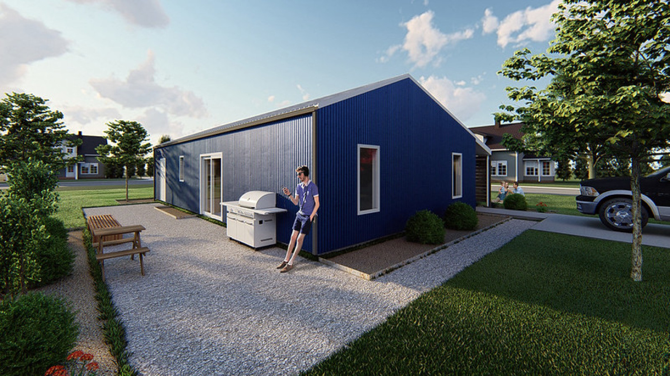 Photo-like drawing of the Kansas team's house, showing the smooth sided exterior and a person leaning against the front of it, with some landscaping around it.