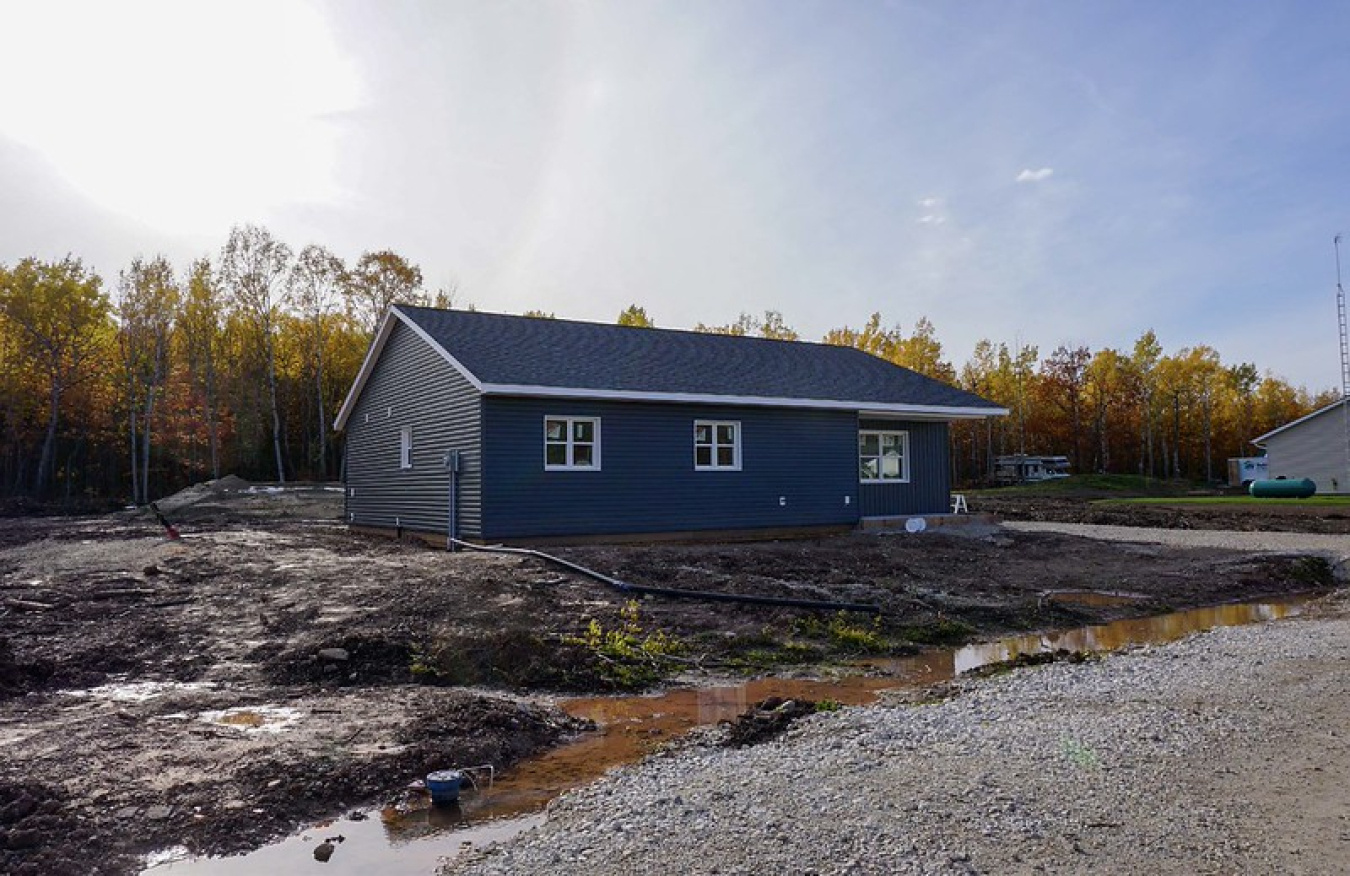 Exterior of the Waterloo team's Build Challenge house, at a distance, with trees behind it and a gravel drive running in front of it.