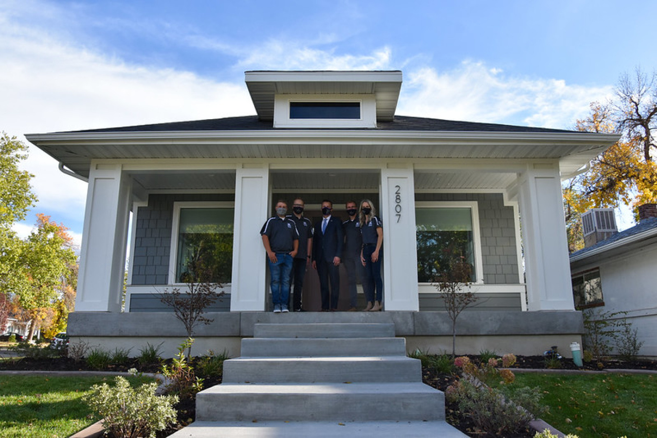 Exterior of the Weber team's Build Challenge house, the front, with several team members standing on the porch in front of the door, between two columns.