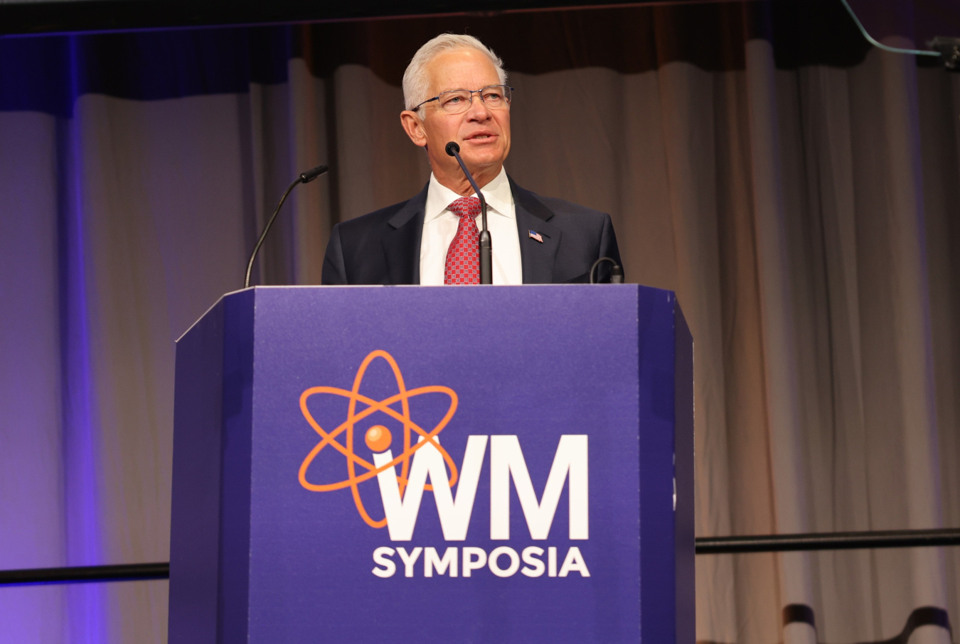 A DOE official in a suit giving a speech behind a podium on a stage