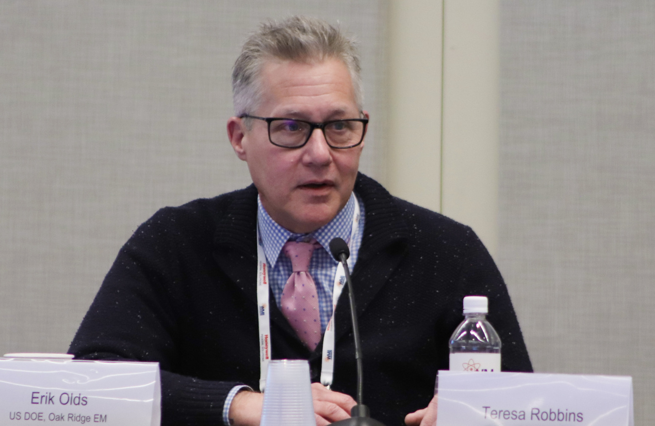 A professional sitting at a panel table on stage at a conference