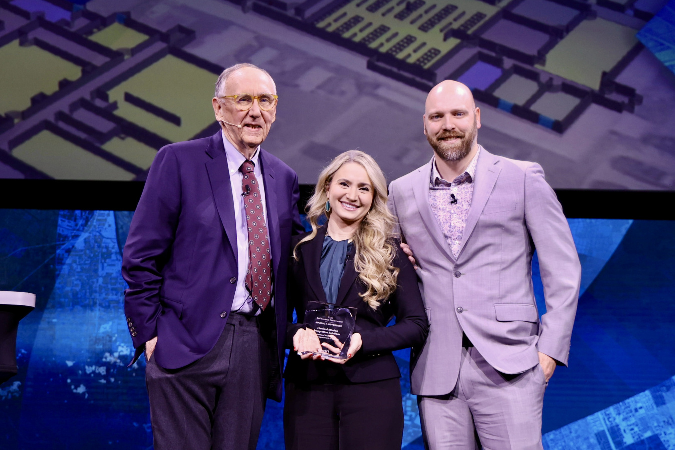 Three professionals on a stage, the one in the middle holds an award