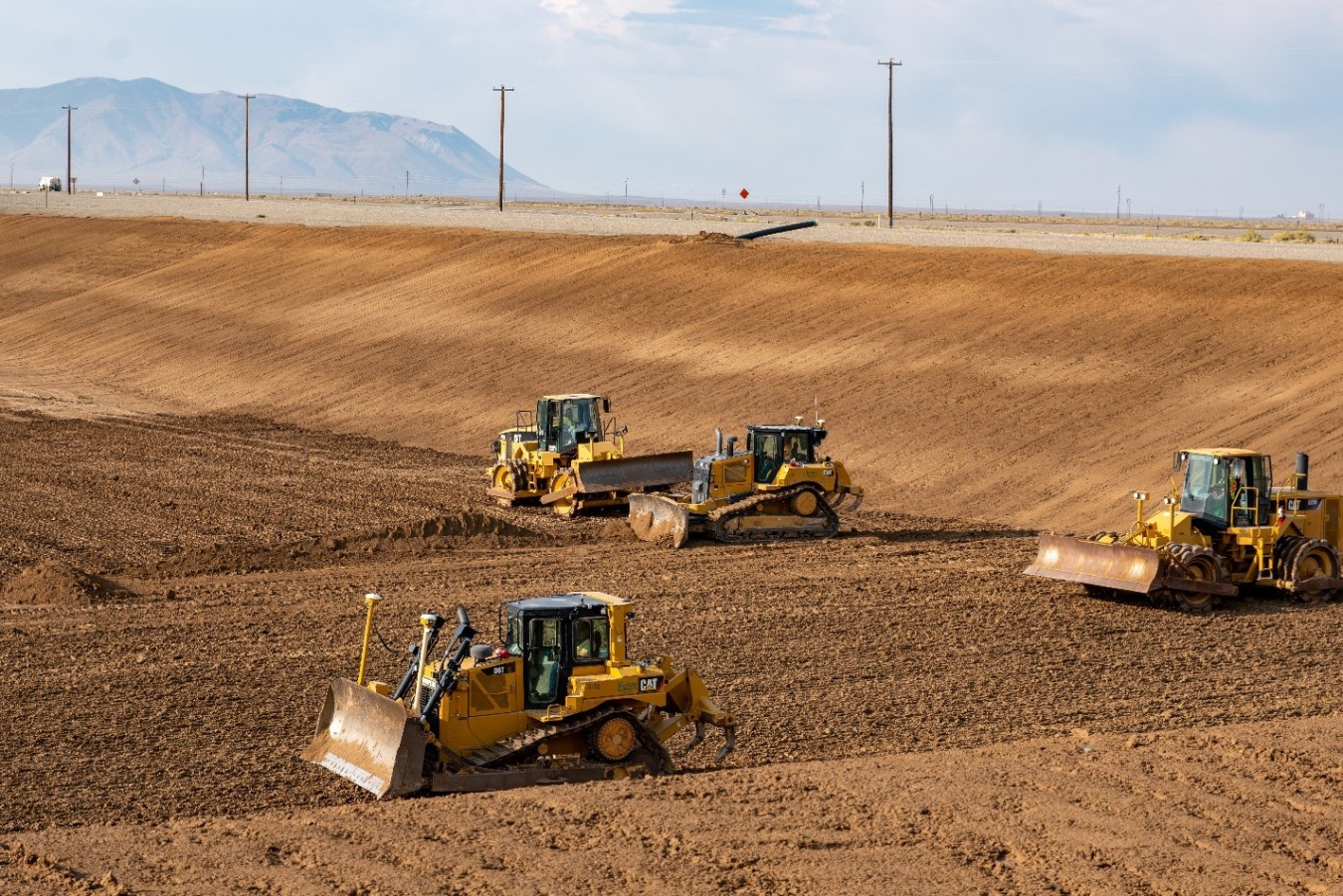 Four yellow construction vehicles within a large dirt filled disposal facility at the Idaho site