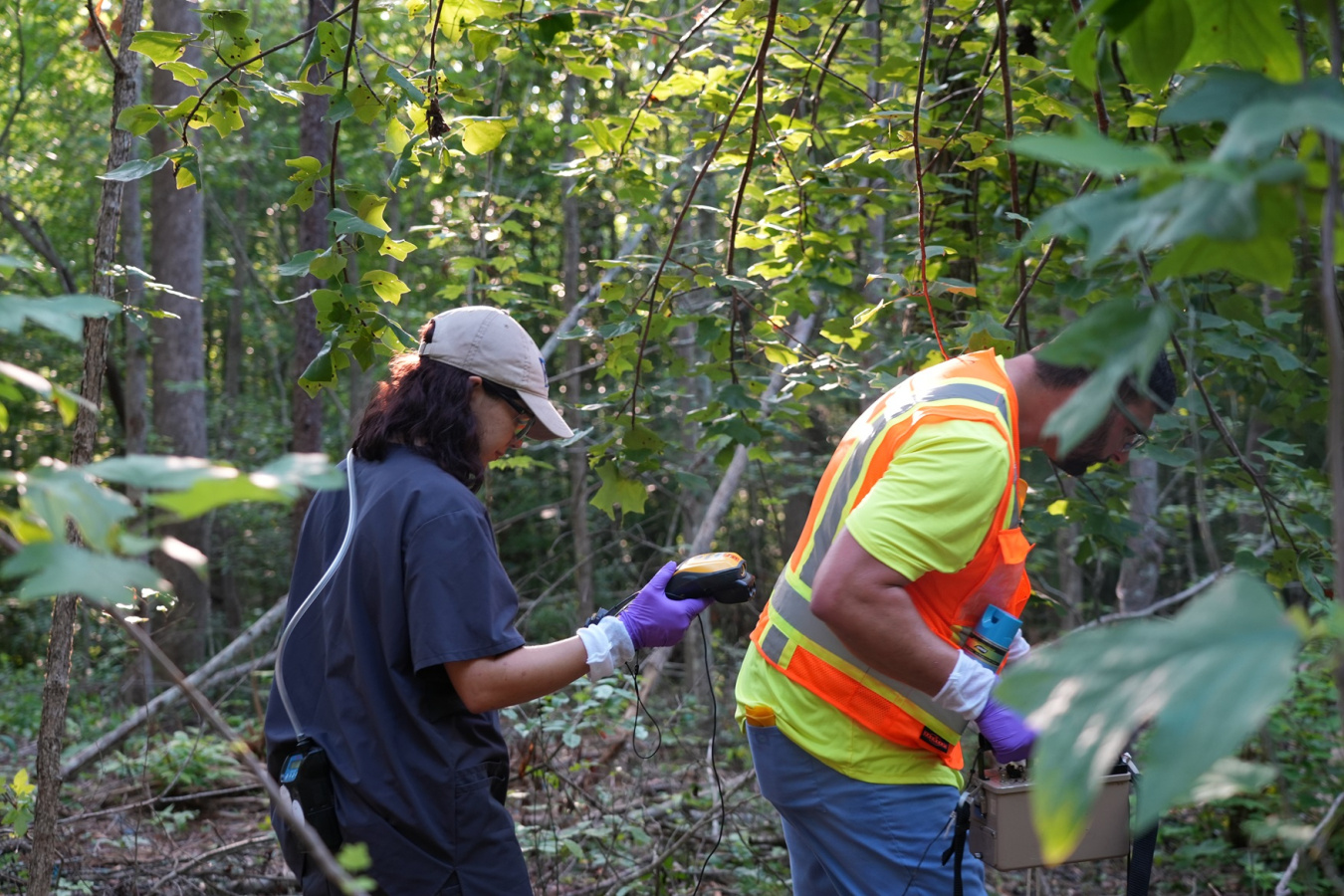 Two individuals conducting radiological surveys at an outdoor scrapyard