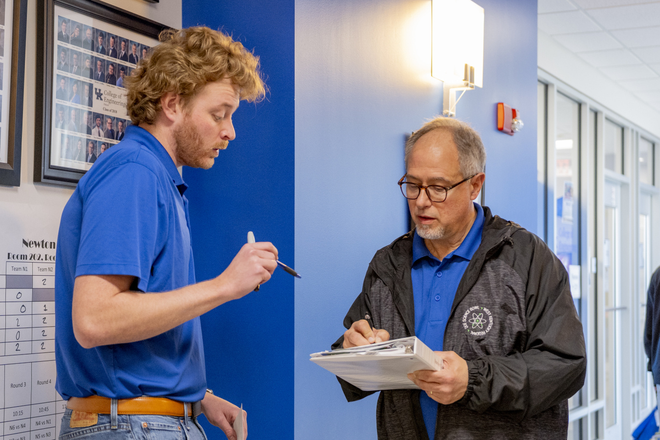Two employees talking to each other, the one on the right is holding a binder that they are both looking at