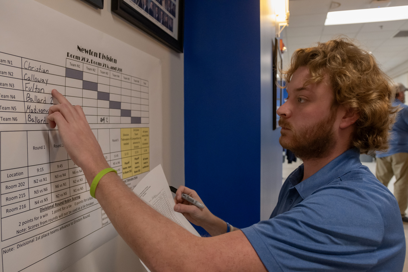 An employee in a blue shirt points at something written on a poster on the wall