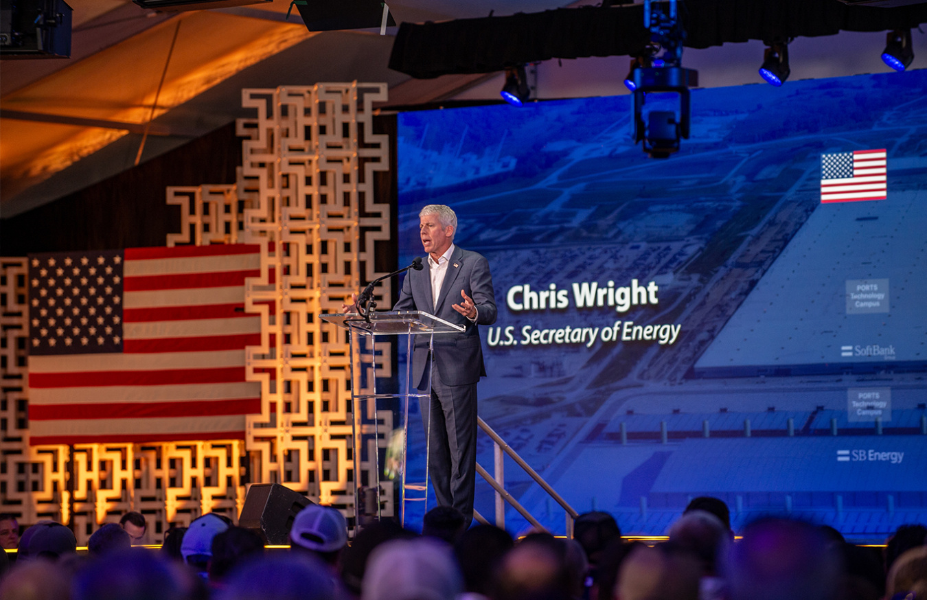 A professional man in a suit standing behind a podium on a stage at a ceremony at the Portsmouth Site